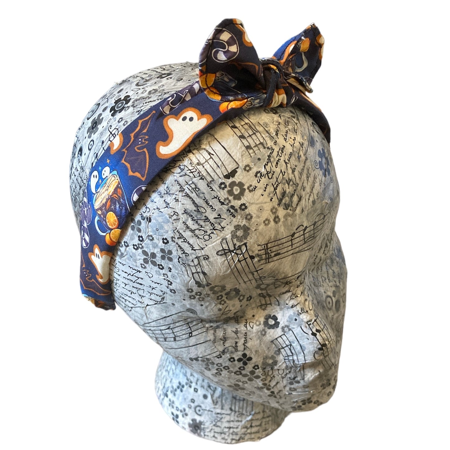 fake head wearing a bow top alice band. Fabric is cotton over a plastic hairband. Fabric pattern has ghost and bat biscuit shapes and cups of orange tea with ghosts floating out.